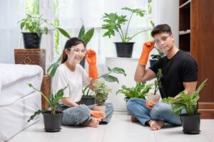 Young man and woman caring for indoor plants in a sunlit living room.