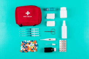 A variety of medical supplies and a red first aid kit on a teal background.