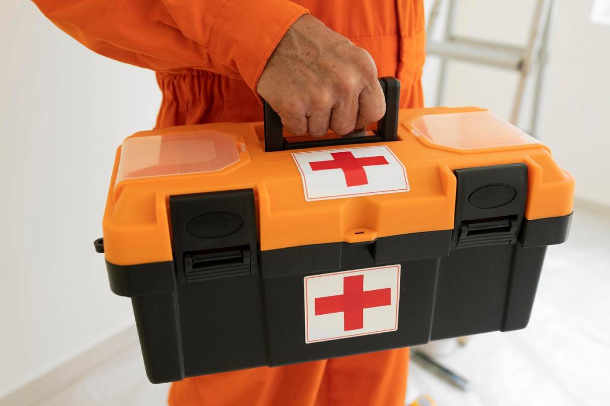A person in an orange jumpsuit holds a large orange first aid kit.